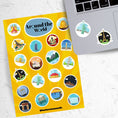 Load image into Gallery viewer, Our Around the World sticker sheet collection has sticker images of iconic travel destinations! This sheet has a yellow background with 20 different stickers. This image shows the sticker sheet next to an open laptop with stickers of the Statue of Liberty and the Eifel Tower applied below the keyboard.
