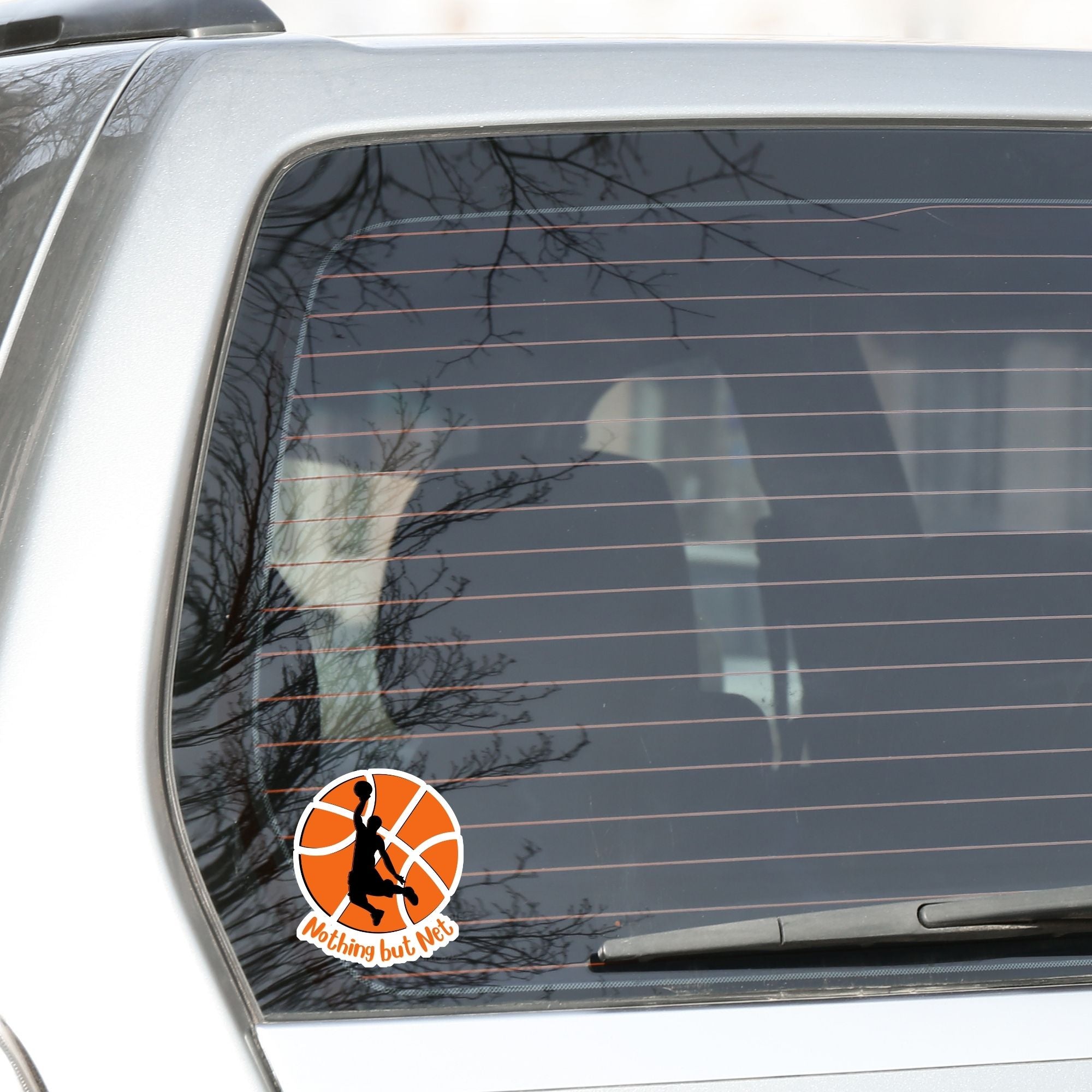 Dunk that basketball! This individual die cut sticker features a silhouette of someone about to dunk a ball, on a basketball background, with the words "Nothing but Net" at the bottom.  This image shows the basketball sticker on the back window of a car.