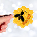 Load image into Gallery viewer, Bee Happy! This individual die-cut sticker is a great motivator. It features a honeycomb background with the silhouette of a bee and the word happy - enough said! This image shows a hand holding the Bee Happy sticker.
