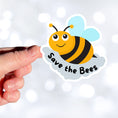 Load image into Gallery viewer, This cute individual die-cut sticker is great for anyone who appreciates our environment or just wants to smell the flowers. The Save the Bees sticker has a happy bumblebee with the saying Save the Bees below. Pair it with our Flowers, Ladybugs and Bees, or Buggin Around sticker sheets for a great gift. This image shows a hand holding the Save the Bees sticker.
