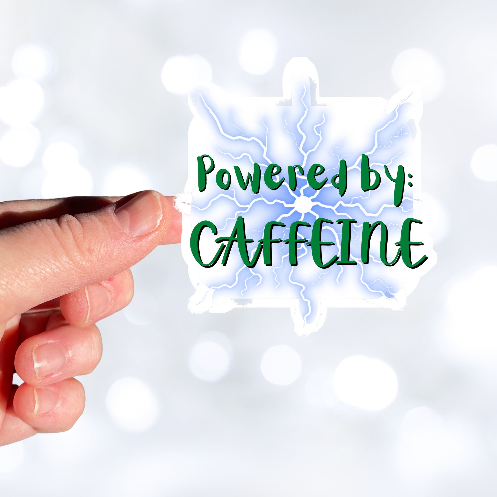 For those who like it, caffeine can be the magic elixir! This individual die-cut sticker has the words Powered by CAFFEINE in green over a background of blue electric/lightning bolts. This image shows a hand holding the Powered by Caffeine sticker.