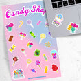 Load image into Gallery viewer, This sticker sheet is filled with stickers of all of your favorite sweet treats! Gumdrops, lollipops, cotton candy, and of course chocolate; this sheet will satisfy everyone's sweet cravings. This image shows the sticker sheet next to an open laptop with stickers of a candy cart and hard candies applied below the keyboard.

