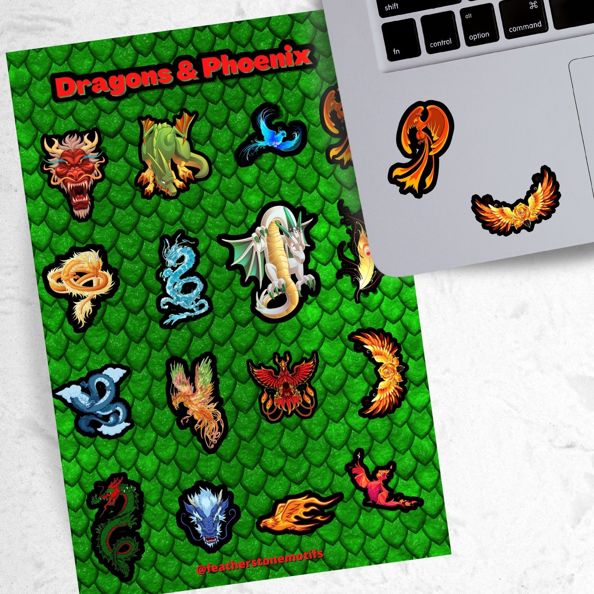 Set on a background of green scales, this sticker sheet has 16 different stickers of dragons and phoenix. This image shows the sticker sheet next to an open laptop with two phoenix stickers applied below the keyboard.