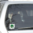 Load image into Gallery viewer, Drummer's, this individual die-cut sticker is for you! It features a drum kit on a green and gray paint splashed background. This drum sticker makes a great gift for anyone who loves to hit the skins. This image shows the drum sticker on the back window of a car.
