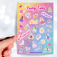 Load image into Gallery viewer, This sticker sheet is filled with stickers of princess's, rainbows, unicorns, and even a frog to kiss (will he turn into a prince?)! This image shows a hand holding a pink sticker reading "Princess" above the sticker sheet.
