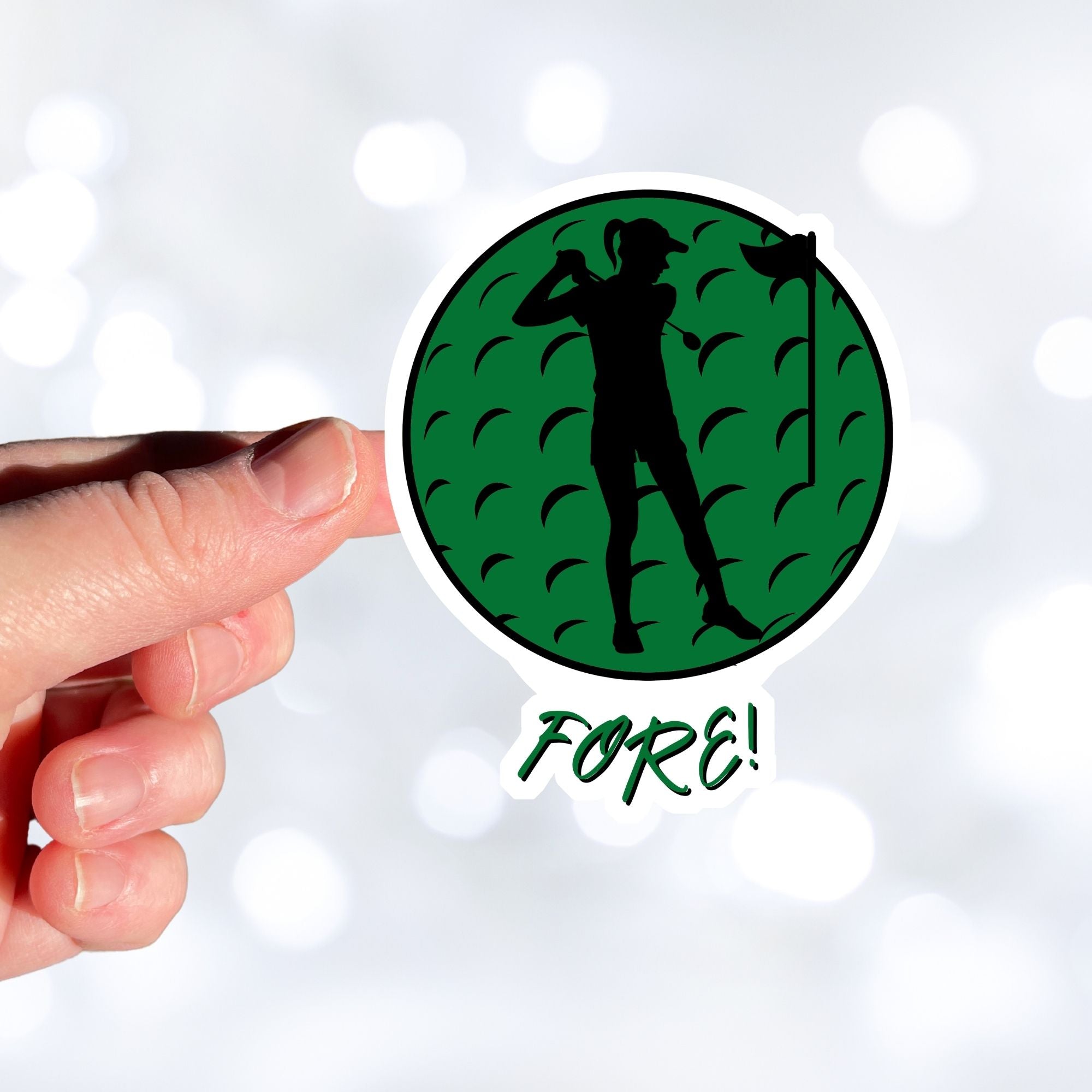 Show your love of golf with this individual die-cut sticker! This sticker shows the silhouette of a golfer with a ponytail about to swing, on a green golf ball background, with the word "Fore!" below.  This image shows a hand holding the golf sticker.
