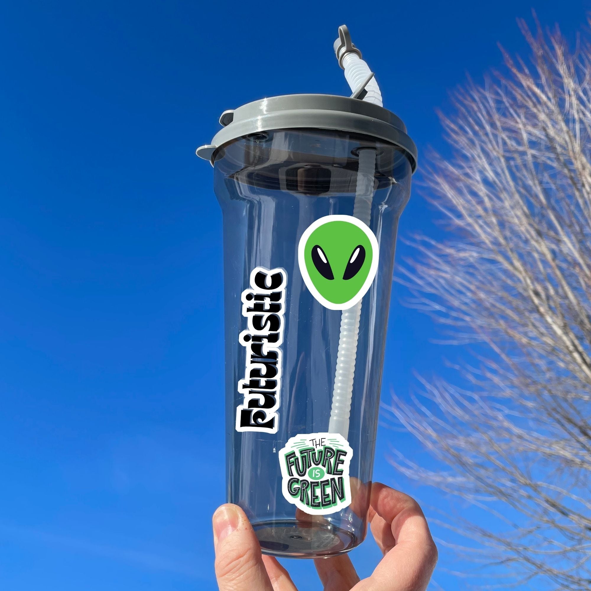 Set on a background of a circuit board, this sticker sheet is filled with futuristic sticker images like rocket ships, flying cars, aliens, and robots, and it has a holographic star overlay! This image shows a water bottle with the sticker sheet header reading "Futuristic", green alien head, and "The Future is Green" stickers applied to it.