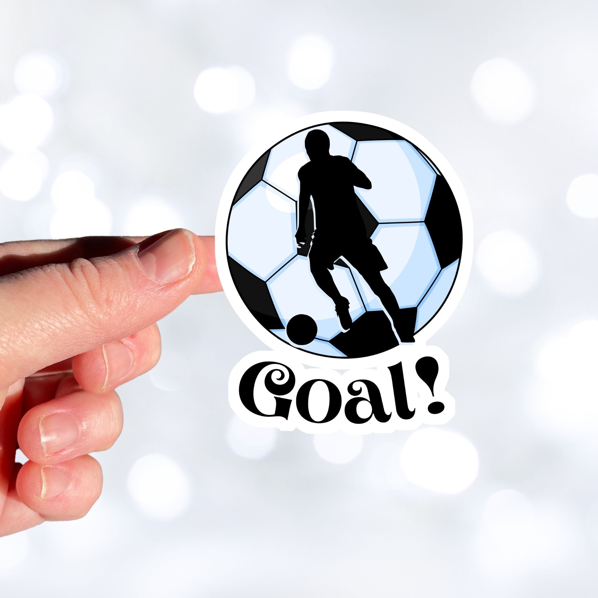 Show your love of soccer, or football, with this individual die-cut sticker! This sticker shows the silhouette of a player about to kick, on a black and white/blue soccer ball background, with the word "Goal!" below. This image shows a hand holding the soccer sticker.