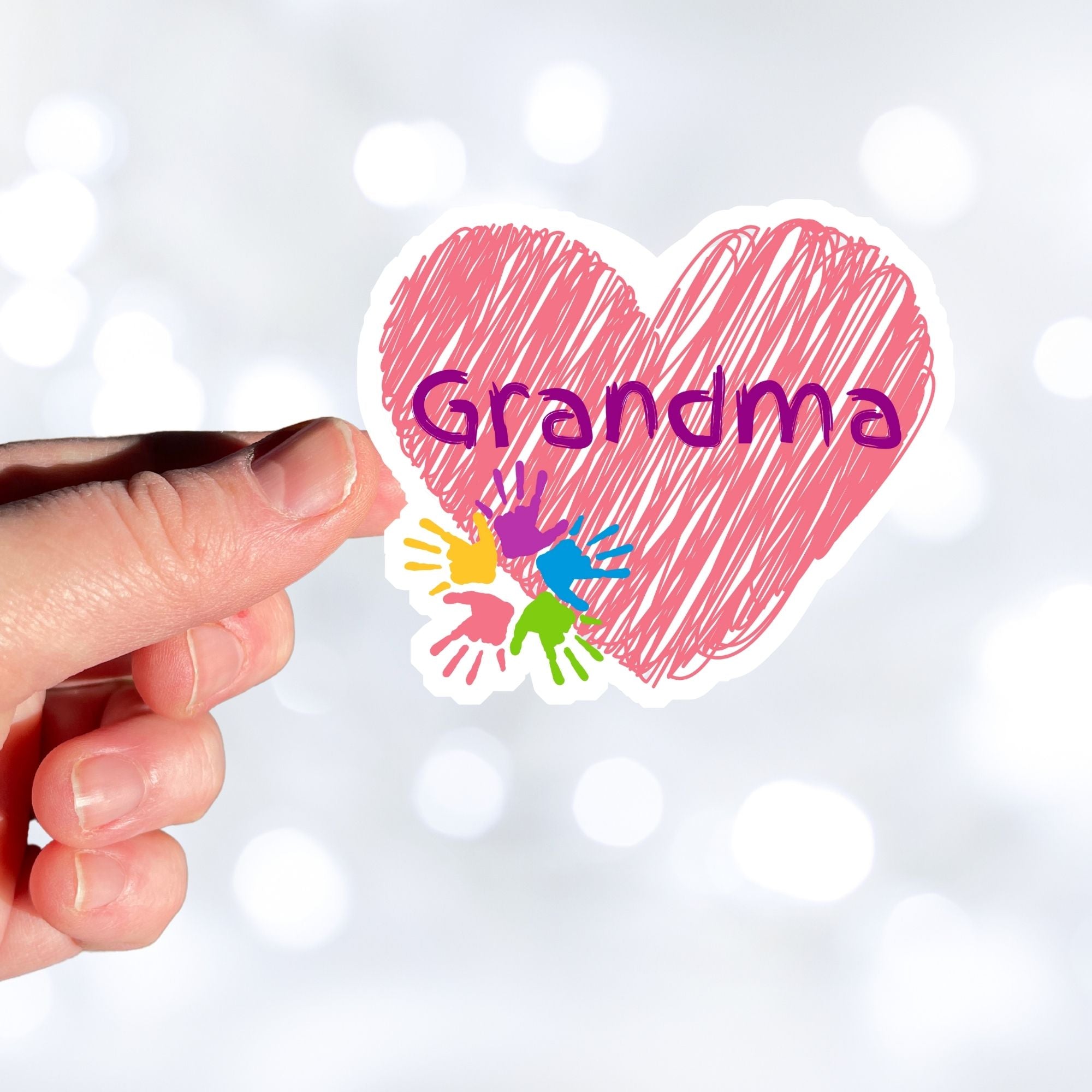 Show how much you love grandma with this individual die-cut sticker. This makes a great gift for grandma, or for all grandma's to proudly show they are a grandmother! This sticker features a red scribbled heart with Grandma written across the middle and 5 small paint hands on the lower left side. This image shows a hand holding the Grandma sticker.