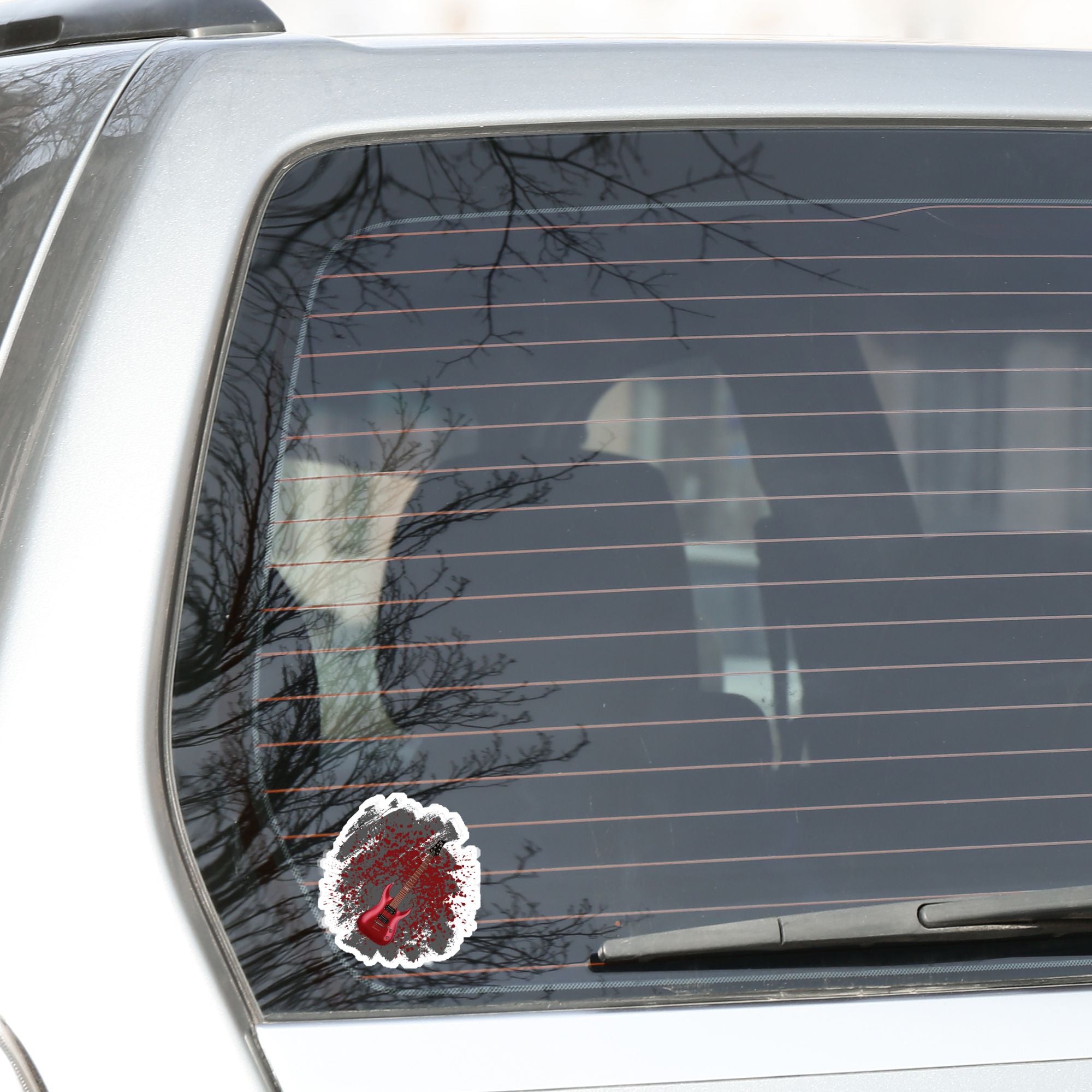 This guitar sticker is great for any guitarist, whether a beginner or a seasoned shredder! This individual die-cut sticker features a burgundy electric guitar on a gray and burgundy paint splattered background. Turn it up!  This image shows the guitar die-cut sticker on the back window of a car.