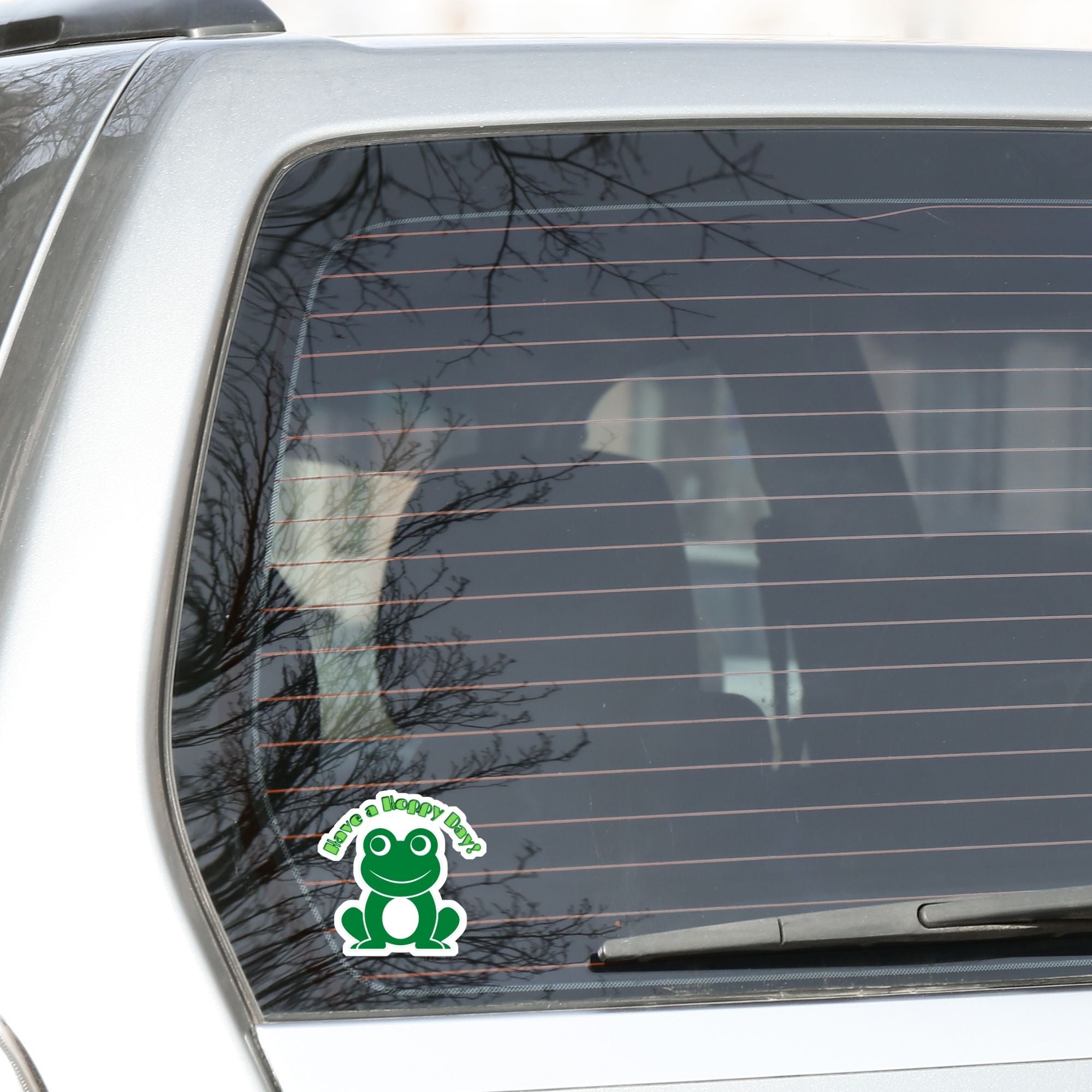 This inspirational sticker features a smiling frog with "Have a Hoppy Day!" written above. This image shows the Have a Hoppy Day sticker on the back window of a car.