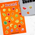 Load image into Gallery viewer, Filled with sticker images of cute fruit, this sticker sheet is sure to put a smile on anyone's face! This image shows the sticker sheet next to an open laptop with stickers of a watermelon slice, a kiwi, and an orange applied below the keyboard.
