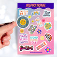 Load image into Gallery viewer, Feel good with these inspirational thoughts as stickers! This sheet has a dozen stickers with inspirational sayings, plus some smaller stickers to help brighten anyone's day. This image shows a hand holding a happy face sticker with the caption "Happy Thoughts" over the sticker sheet.
