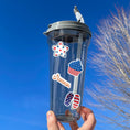 Load image into Gallery viewer, Celebrate summer, and the 4th of July in the USA. This sticker sheet has all of your favorite summer time foods like BBQing, burgers, hot dogs, and corn on the cob. Plus fireworks and red, white, and blue images. This image shows a water bottle with four summer time and patriotic stickers applied to it.
