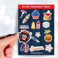 Load image into Gallery viewer, Celebrate summer, and the 4th of July in the USA. This sticker sheet has all of your favorite summer time foods like BBQing, burgers, hot dogs, and corn on the cob. Plus fireworks and red, white, and blue images. This image shows a hand holding a sticker of a grill (or BBQ) over the sticker sheet.

