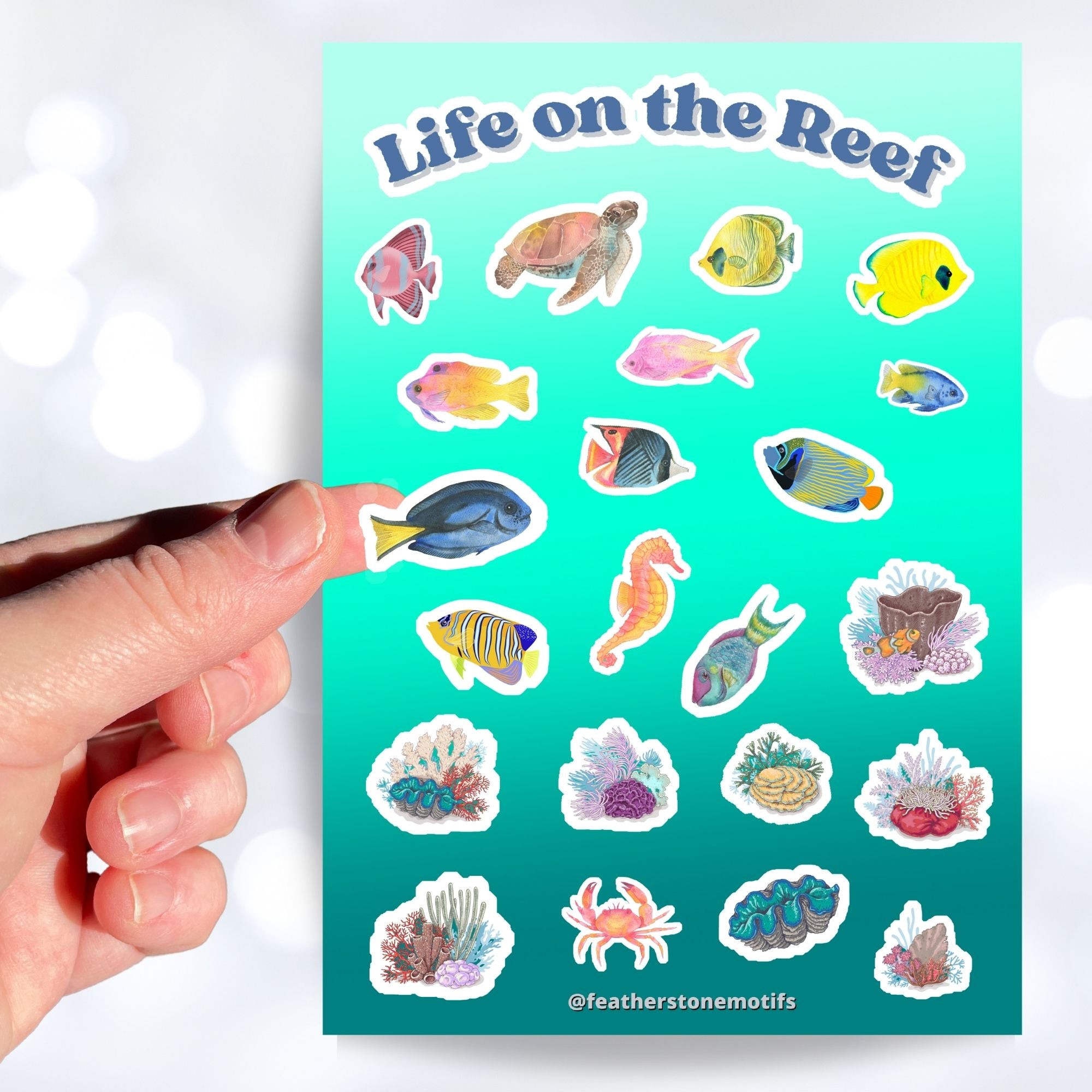 Teaming with sea life, this sticker sheet is filled with sticker images of fish, sea turtles, and coral! Take the reef with you anywhere with these beautiful stickers. This image shows a hand holding a sticker of a blue tang above the sticker sheet.
