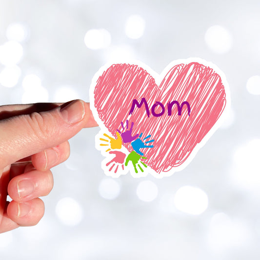 Show how much you love your mom with this individual die-cut sticker. This makes a great gift for mom, or for all mom's to proudly show they are a mother! This sticker features a pink scribbled heart with Mom written across the middle and 5 small paint hands on the lower left side. This image shows a hand holding the Mom sticker.