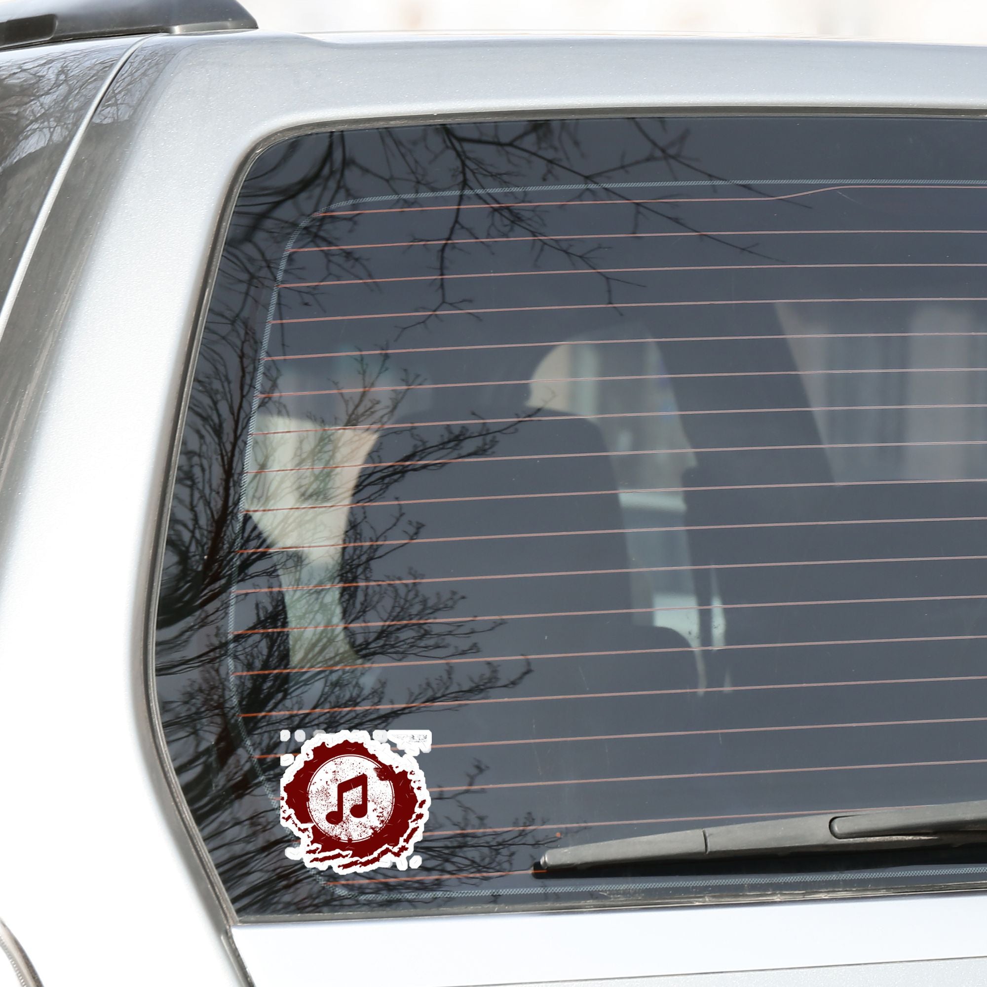 This individual die-cut sticker features a double music note in brown with a paint splattered background. Perfect for performers and music lovers alike! This image shows the music note sticker on the back window of a car.