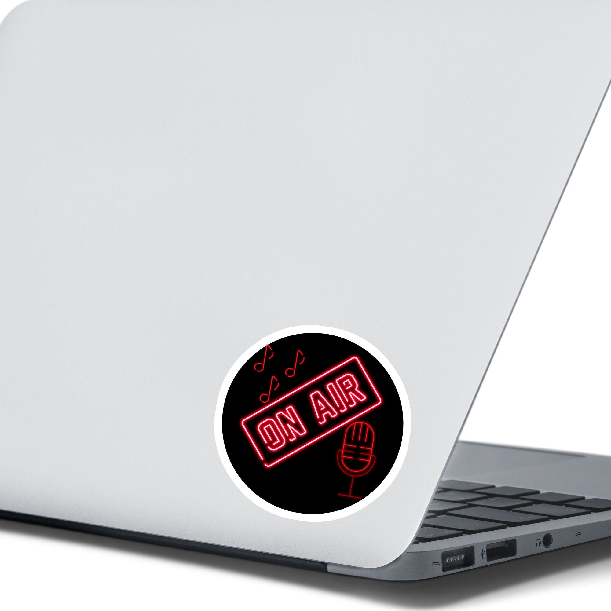Music, TV, Podcast, or even Amateur Radio - this sticker is great for anyone who is On Air! This individual die-cut sticker is in neon red with the words On Air above a microphone with music notes above. Please note that the large version of this sticker is on a white background and cut around the image, and the small version is on a black circle. This image shows a small On Air sticker on the back of an open laptop.