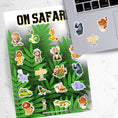 Load image into Gallery viewer, Who's ready to go "On Safari"? This jungle themed sticker sheet has images of your favorite jungle creatures, kid explorers, and all the things you need for your next jungle adventure!  This image shows the On Safari sticker sheet next to a laptop with stickers of a gorilla, tiger, and Safari sign applied below the keyboard.
