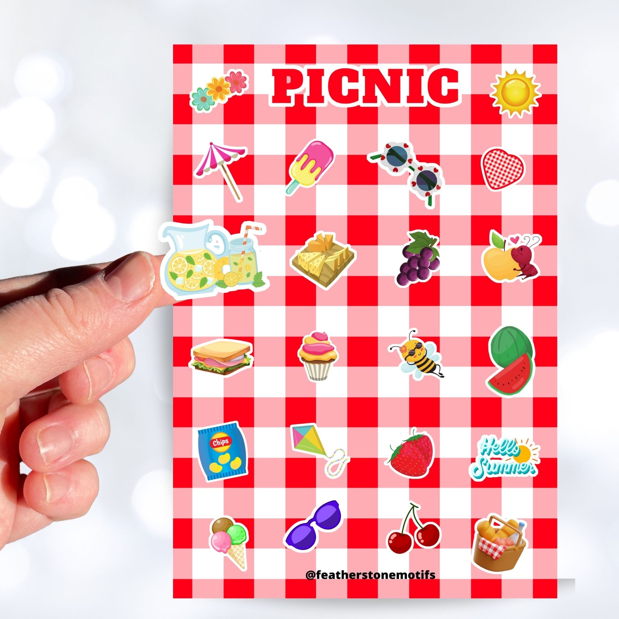 Pack the picnic basket and grab a blanket; we're going on a picnic! This sticker sheet has sticker images of all your favorite picnic foods and activities like sandwiches, fruit, ice cream, and lemonade all on a red and white checked tablecloth background. This image shows a hand holding a sticker of lemonade in a pitcher and glass above the sticker sheet.