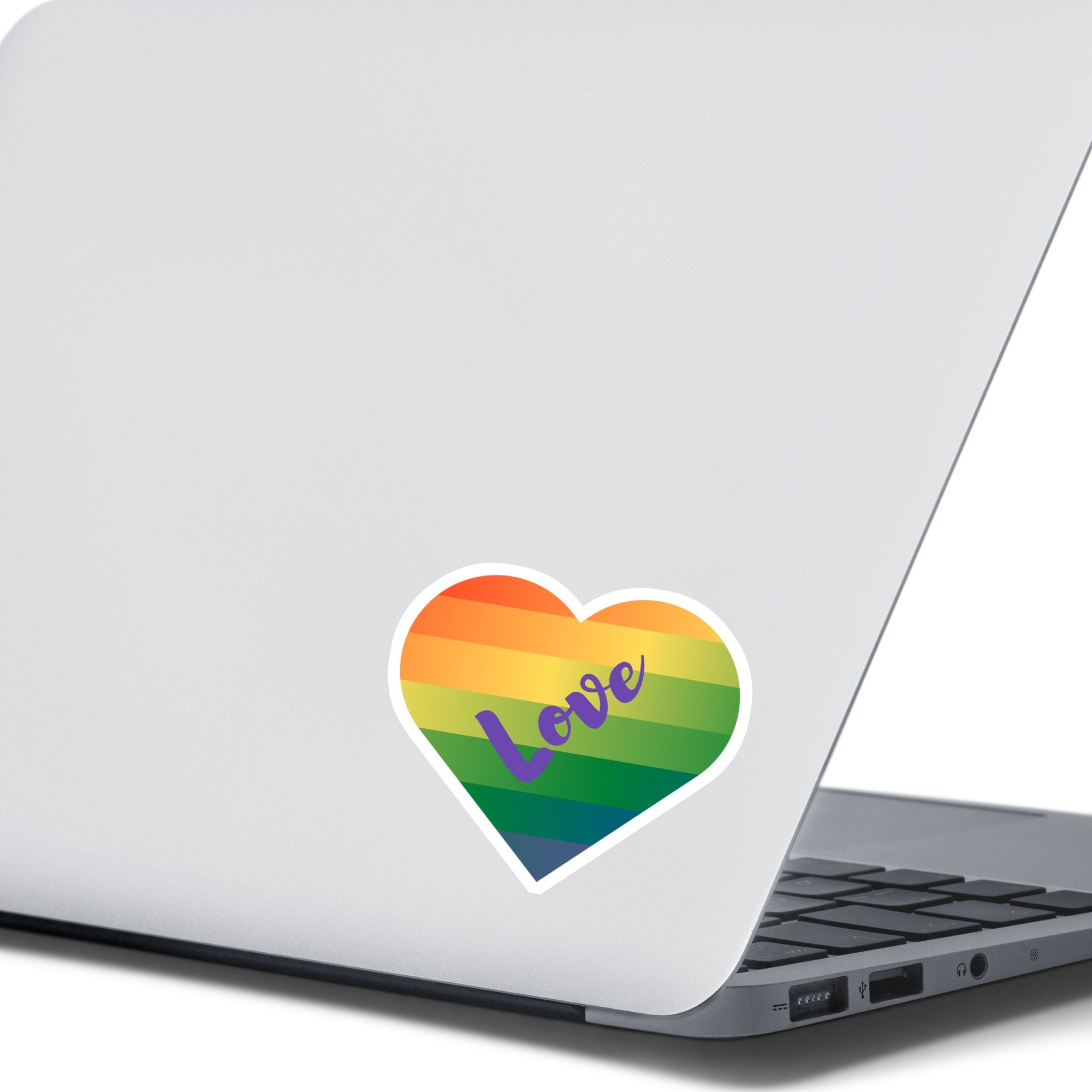 This individual die-cut sticker features a heart shape with graduated colors from orange at the top to blue at the bottom, and the word love written across. Perfect for the people you love! This image shows the Love Heart sticker on the back of an open laptop.