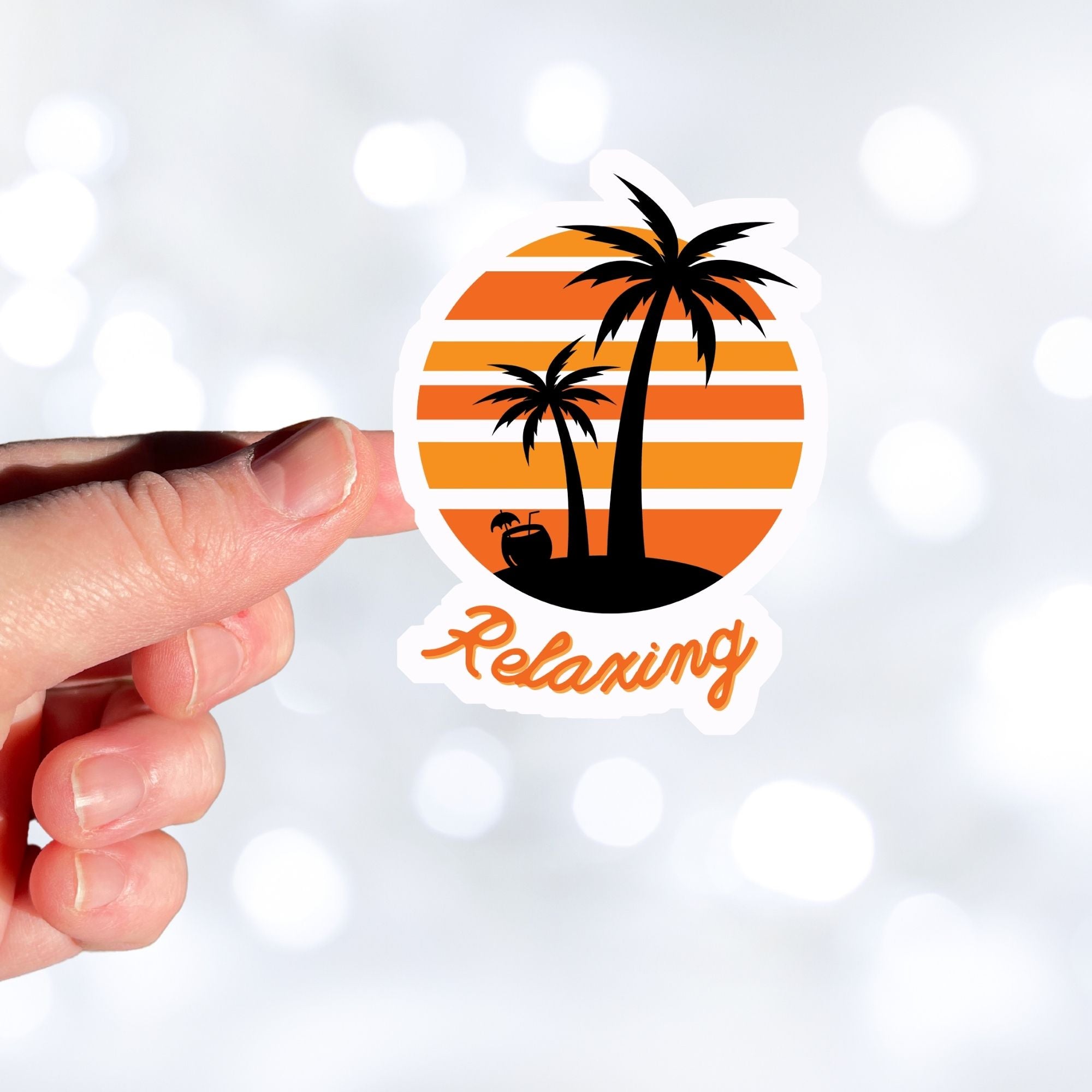 Grab your favorite beverage and relax under the palm trees! This individual die-cut sticker features two palm trees and an umbrella drink in a coconut shell, on an orange and white gradient background, with the word "Relaxing" below. This image shows a hand holding the relaxing sticker.