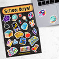 Load image into Gallery viewer, Reading, writing, and arithmetic; this sticker sheet is perfect for students, or educators, of all ages! It's filled with stickers showing all aspects of school - books, globe, crayons, backpacks, and of course a mortarboard / graduation cap! This image shows the sticker sheet next to an open laptop with a globe sticker and a sticker with books, apples, and a pencil applied to it.
