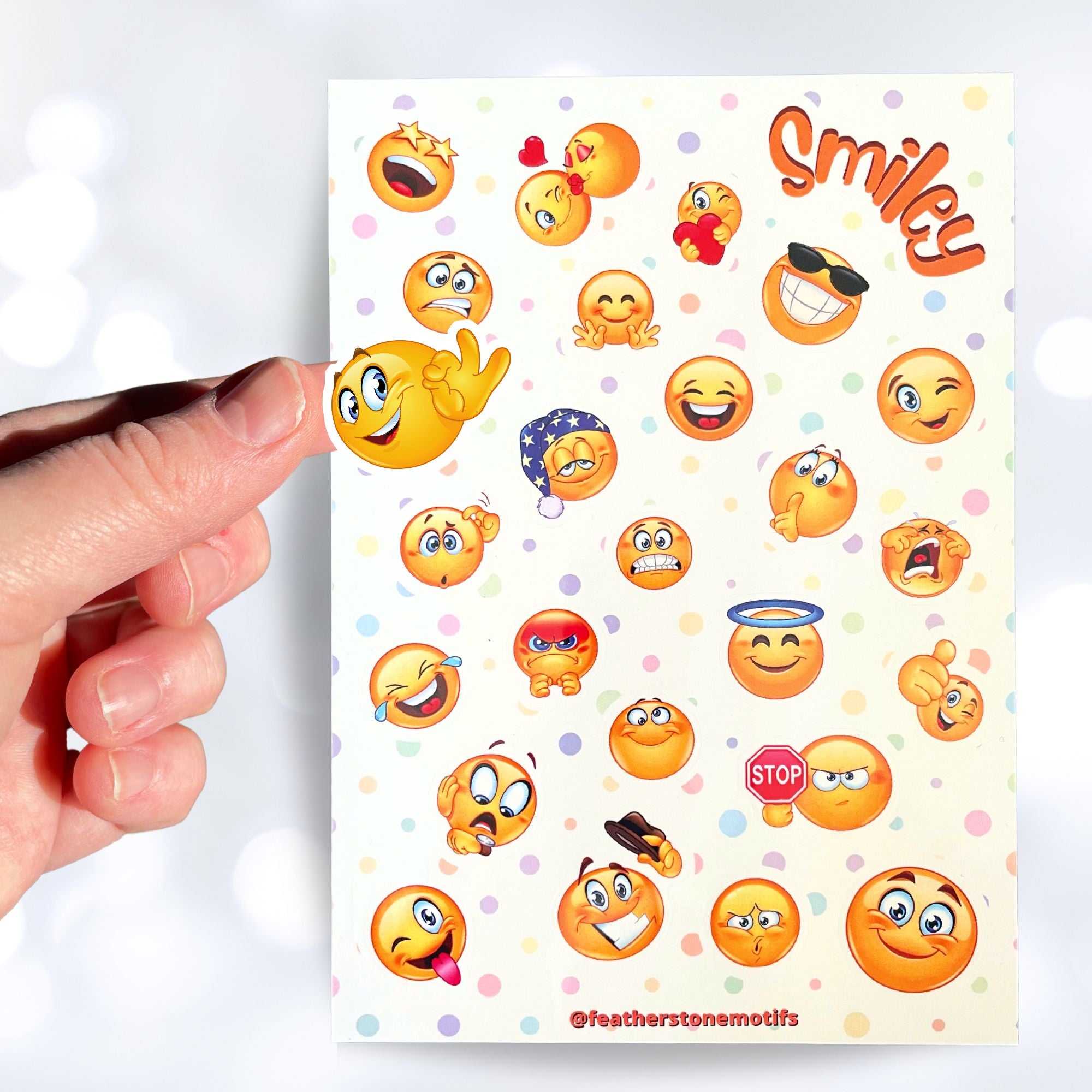 This sticker sheet features all your favorite smiley emojis! It's enough to make anyone smile! This image shows a hand holding a smiley face sticker above the sticker sheet.