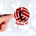 Load image into Gallery viewer, Show your love of volleyball with this individual die-cut sticker! This sticker shows the silhouette of a player with a ponytail about to spike the ball, on a maroon and white volleyball background, with the words "Spike it!" below. This image shows a hand holding the volleyball sticker.
