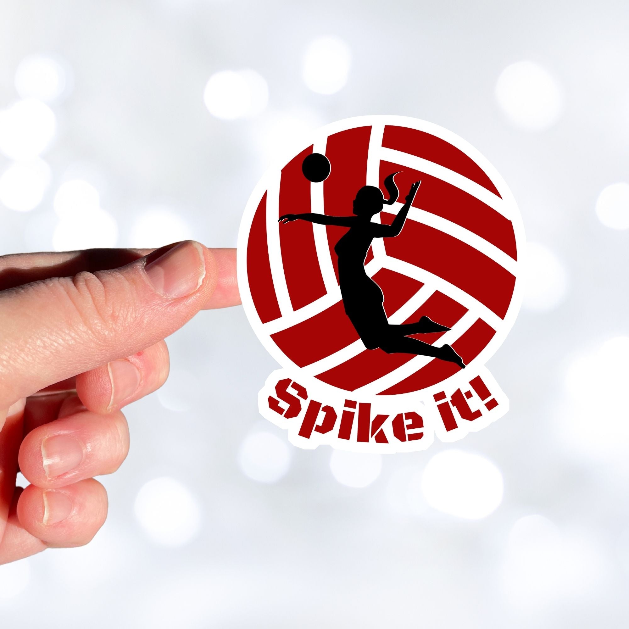 Show your love of volleyball with this individual die-cut sticker! This sticker shows the silhouette of a player with a ponytail about to spike the ball, on a maroon and white volleyball background, with the words "Spike it!" below. This image shows a hand holding the volleyball sticker.