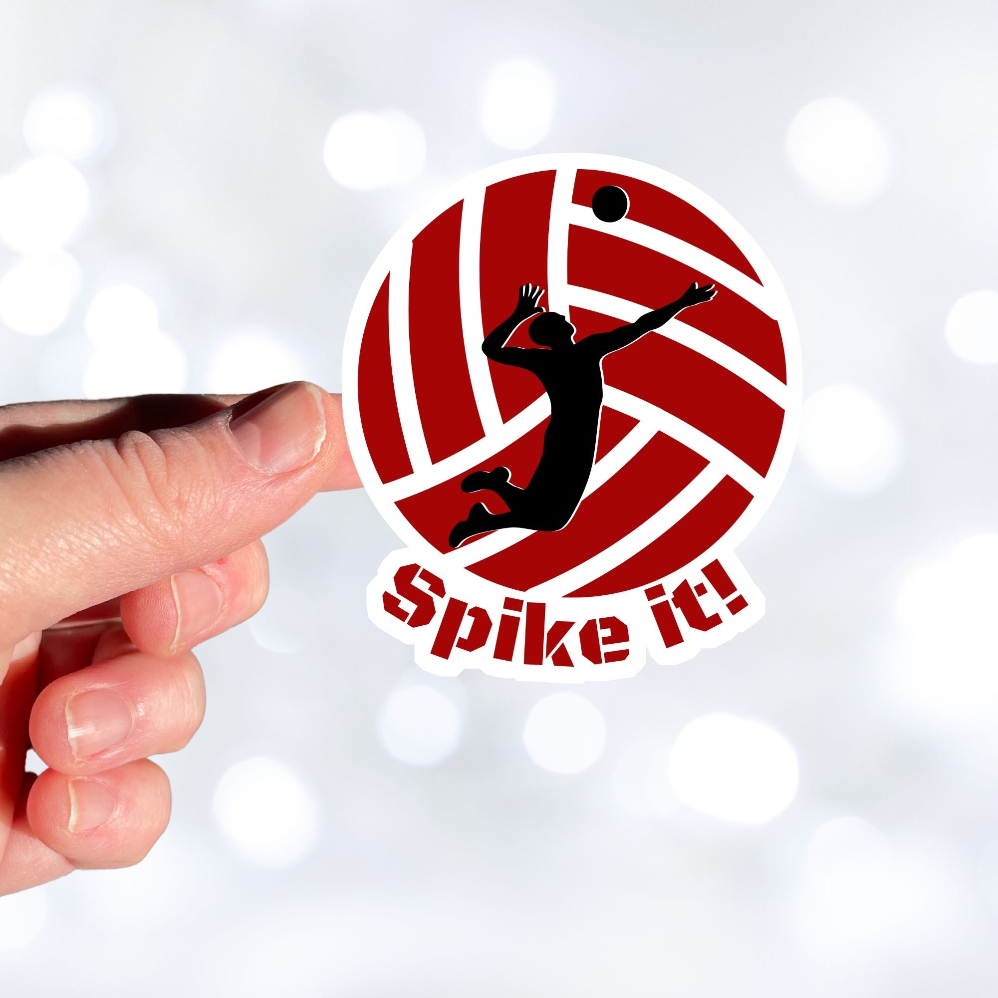 Show your love of volleyball with this individual die-cut sticker! This sticker shows the silhouette of a player about to spike the ball, on a maroon and white volleyball background, with the words "Spike it!" below. This image shows a hand holding the volleyball sticker.