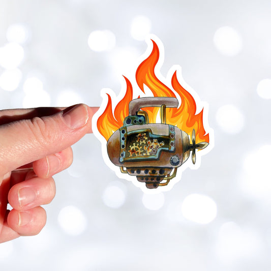 This individual die-cut steampunk sticker features a brown engine with a cutaway to show the gears inside, on a background of yellow, orange, and red flames. This image shows the steampunk engine sticker being held above a white background.