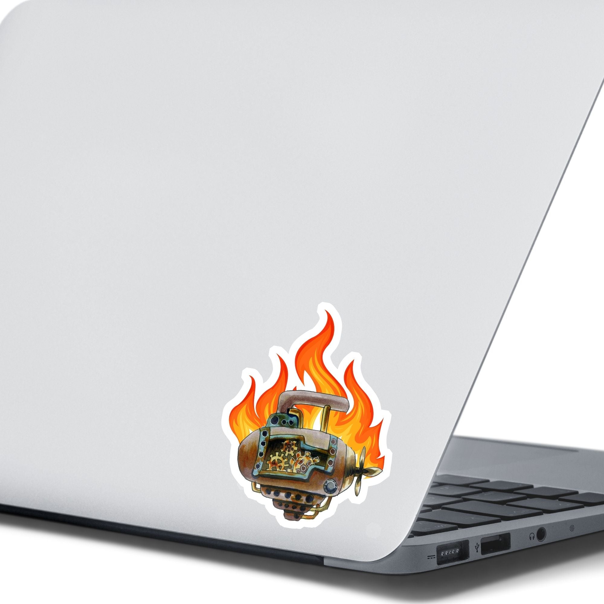 This individual die-cut steampunk sticker features a brown engine with a cutaway to show the gears inside, on a background of yellow, orange, and red flames. This image shows the steampunk engine sticker on the back of an open laptop.