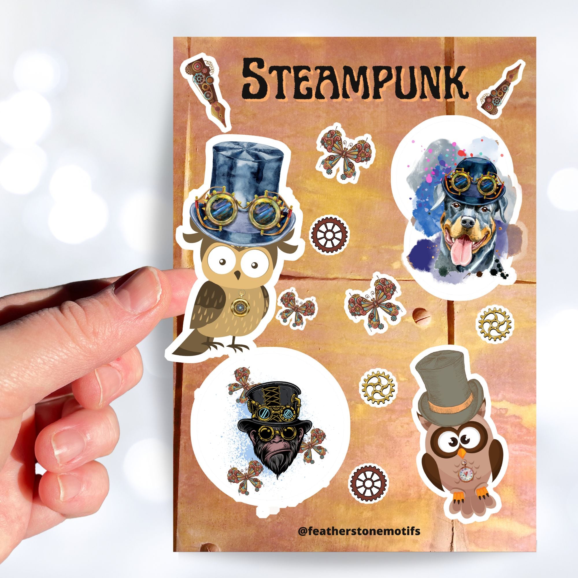 This Steampunk sticker sheet features four large animal stickers: Mr. and Mrs. Owl, Steampunk Monkey, and Steampunk Rotty (Rottweiler) along with smaller miscellaneous gear, butterfly, and pen stickers.  This image shows a hand holding the Mrs. Owl sticker above the sticker sheet. Mrs. Owl is an owl with a steampunk hat and goggles and a clock necklace.