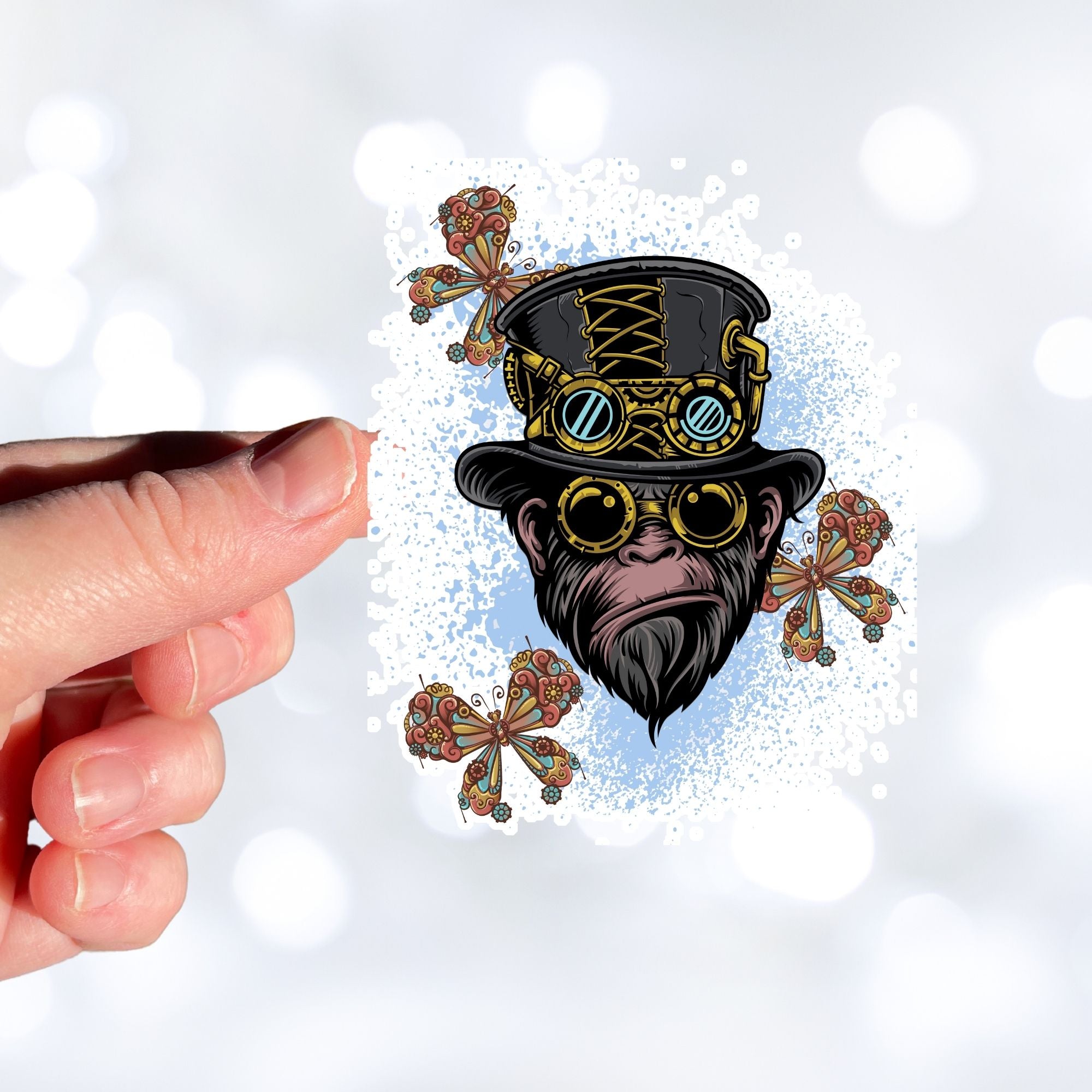 Steampunk Monkey has his own version of a steampunk hat and goggles, plus he is wearing goggles and surrounded by three steampunk butterflies. All on a blue and white background. This image shows a hand holding the steampunk monkey sticker.