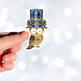 Load image into Gallery viewer, Mrs. Owl is sporting a steampunk hat with goggles and she has her own steampunk watch necklace. This image shows the Mrs. Owl sticker being held above a white background.
