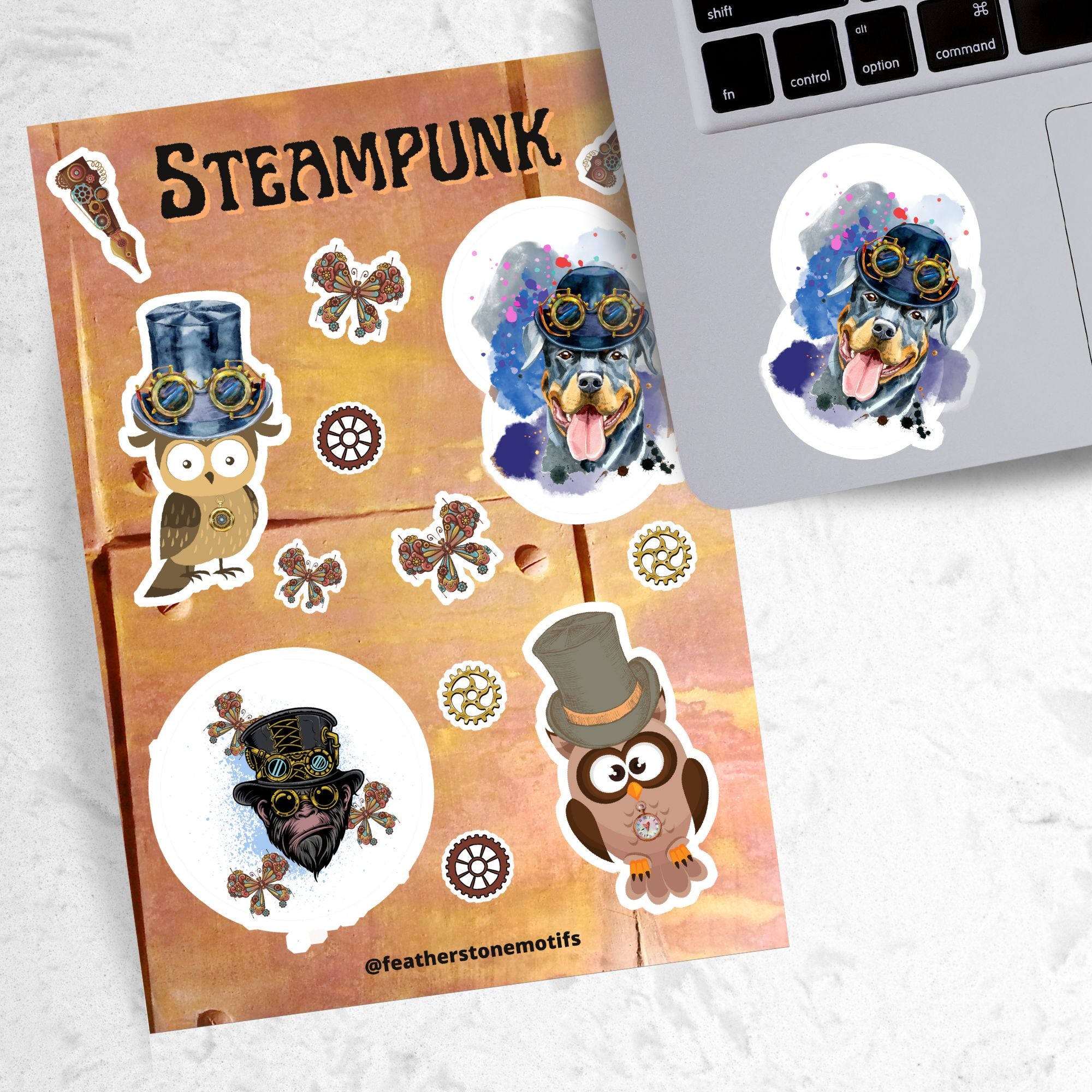 This Steampunk sticker sheet features four large animal stickers: Mr. and Mrs. Owl, Steampunk Monkey, and Steampunk Rotty (Rottweiler) along with smaller miscellaneous gear, butterfly, and pen stickers.  This image shows the sticker sheet next to an open laptop with the Steampunk Rotty sticker applied below the keyboard. The steampunk Rotty sticker is a Rottweiler  wearing a steampunk hat with goggles and a pastel background..