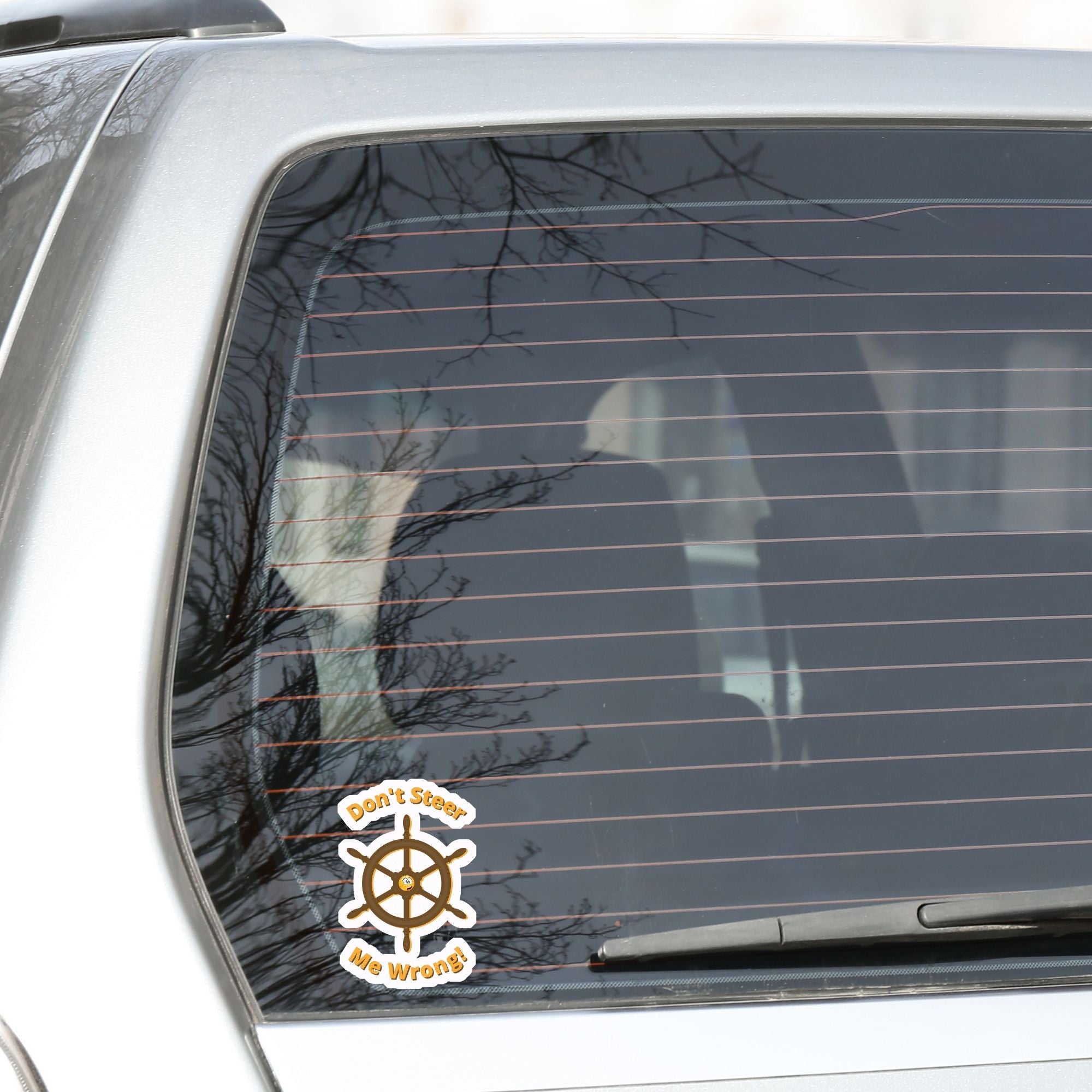 Don't Steer Me Wrong - good words to live by! This individual die-cut sticker features a wooden ship's wheel (tiller) with a shocked emoji face in the center and the words "Don't Steer Me Wrong!" above and below. This image shows the sticker on the back window of a car.