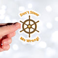 Load image into Gallery viewer, Don't Steer Me Wrong - good words to live by! This individual die-cut sticker features a wooden ship's wheel (tiller) with a shocked emoji face in the center and the words "Don't Steer Me Wrong!" above and below. This image shows a hand holding the sticker.
