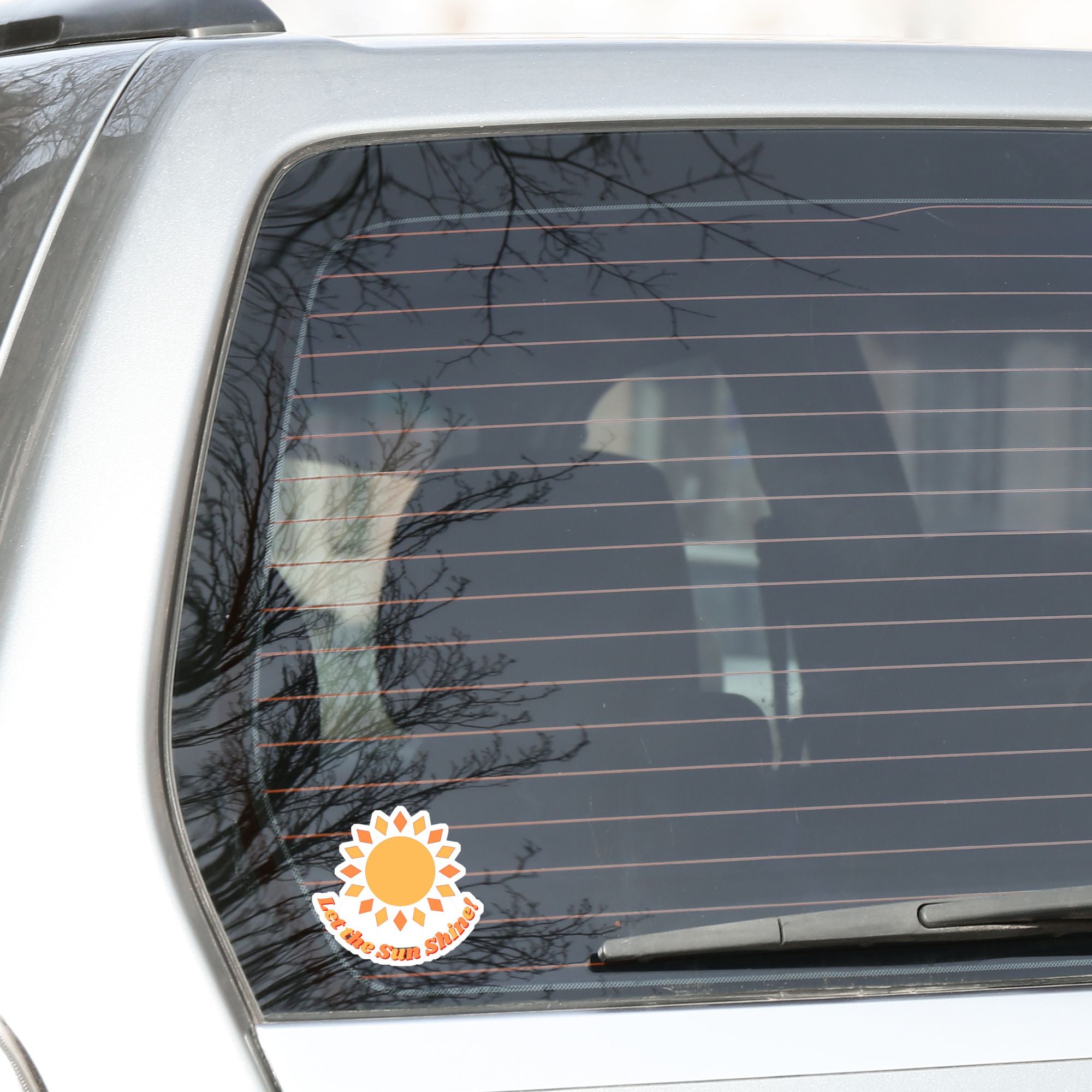 Let the Sun Shine! This bright and fun individual die-cut sticker features a yellow and orange sun with the words "Let the Sun Shine!" below. This image shows the Let the Sun Shine! die-cut sticker on the back window of a car.