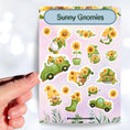 Load image into Gallery viewer, Sunflowers and Gnomes; what a perfect combination! This sticker is filled with stickers of sunflowers and gnomes with sunflowers.  This image shows a hand holding a gnome driving a car full of sunflowers held above the sticker sheet.
