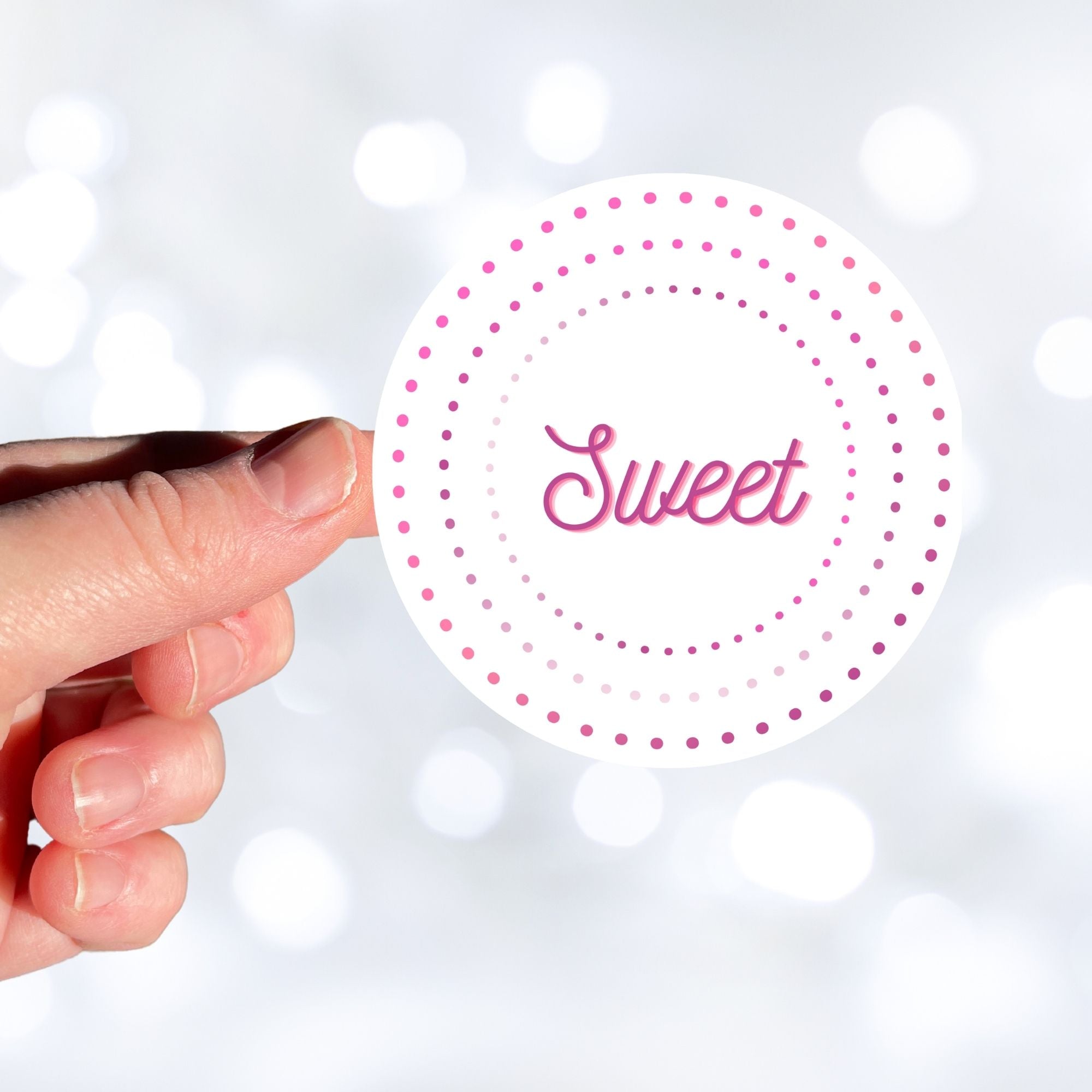 This round individual die-cut sticker is Sweet! It features the word Sweet in the center surrounded by pink and purple circular dots. This makes a great gift for anyone you're sweet on! This image shows a hand holding the Sweet sticker.