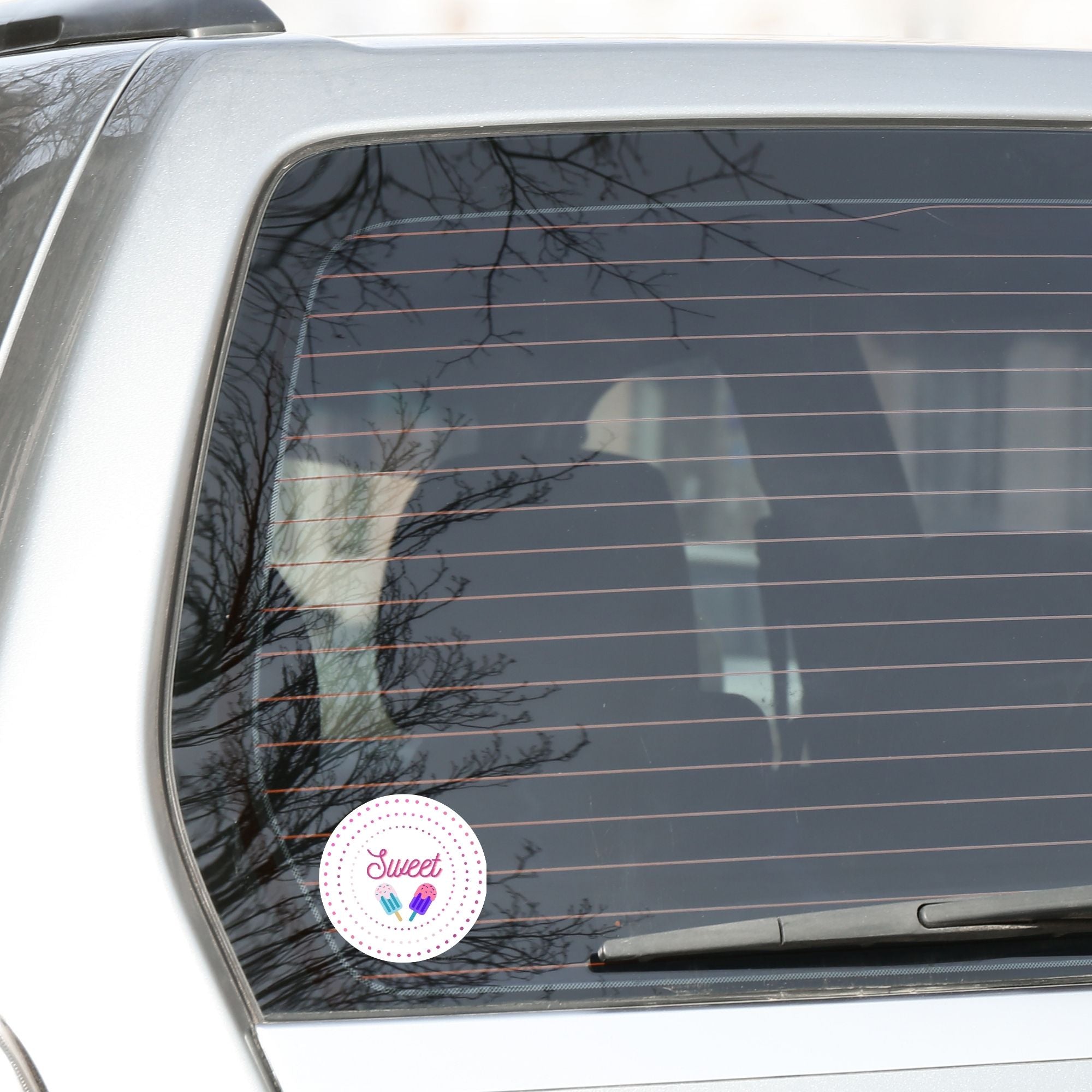 Sweet as Ice Cream! This round individual die-cut sticker has the word Sweet with two ice cream bars in the center surrounded by pink and purple circular dots. This makes a great gift for your sweetie! This image shows the Sweet - Ice Cream die-cut sticker on the back window of a car.