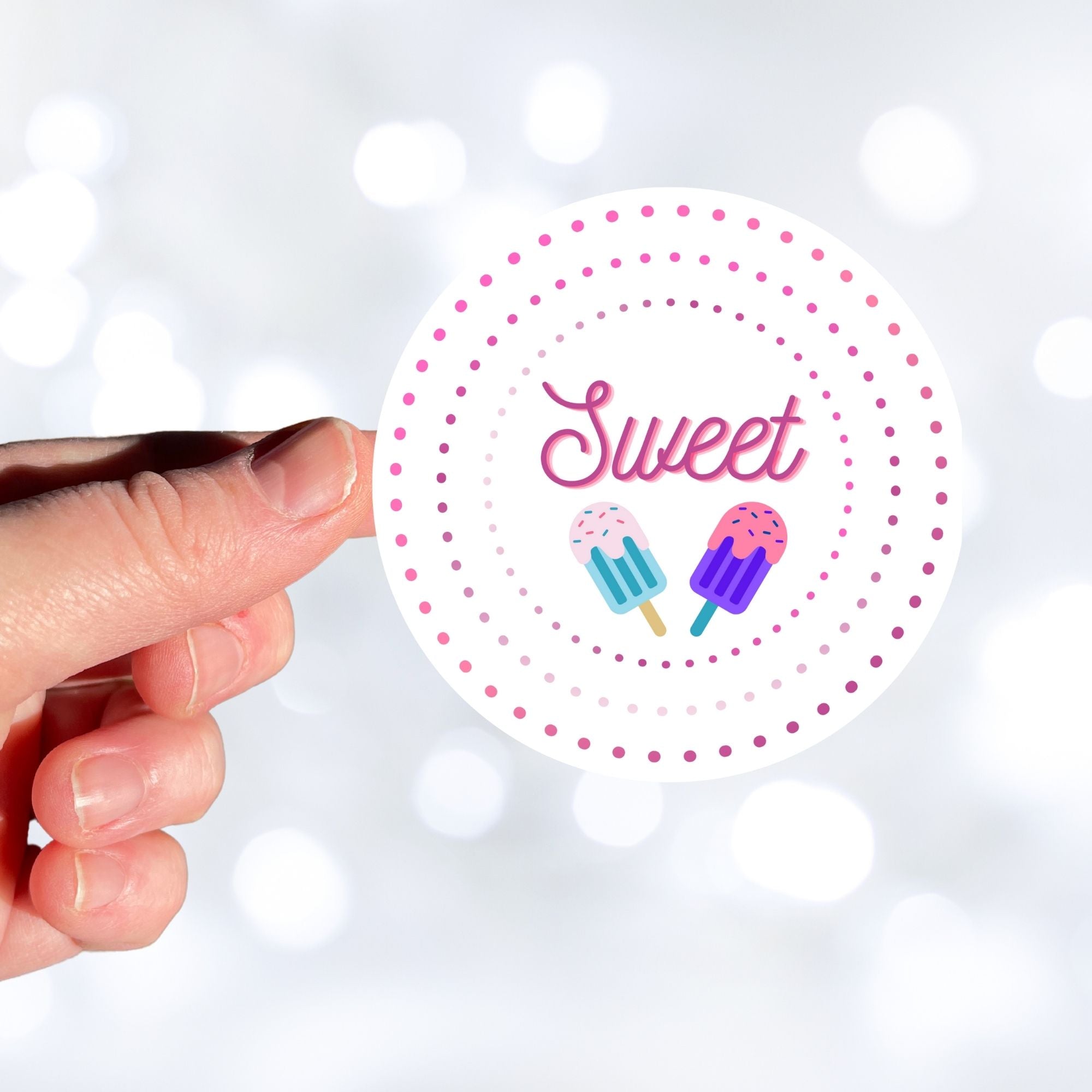 Sweet as Ice Cream! This round individual die-cut sticker has the word Sweet with two ice cream bars in the center surrounded by pink and purple circular dots. This makes a great gift for your sweetie! This image shows a hand holding the Sweet - Ice Cream sticker.