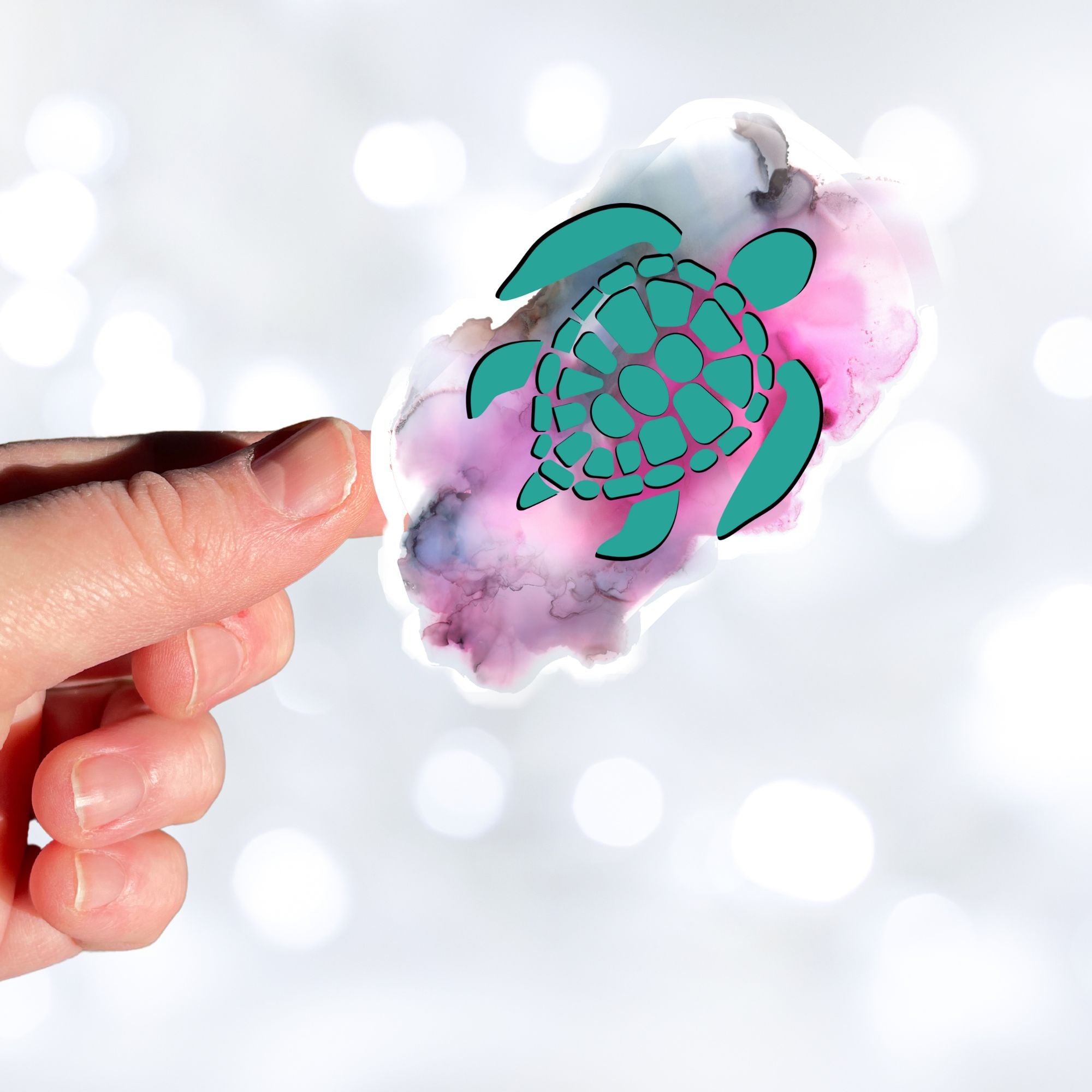 This individual die-cut sticker features a green tribal style turtle on a gray and pink cloudy background. This image shows a hand holding the turtle sticker.