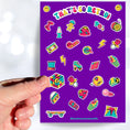 Load image into Gallery viewer, This sticker sheet is filled with images of items from the 70's, 80's, and 90's. Sticker images include a troll doll, roller skate, Rubik's cube, and a skateboard. This image shows a hand holding a Rubik's cube above the sticker sheet.
