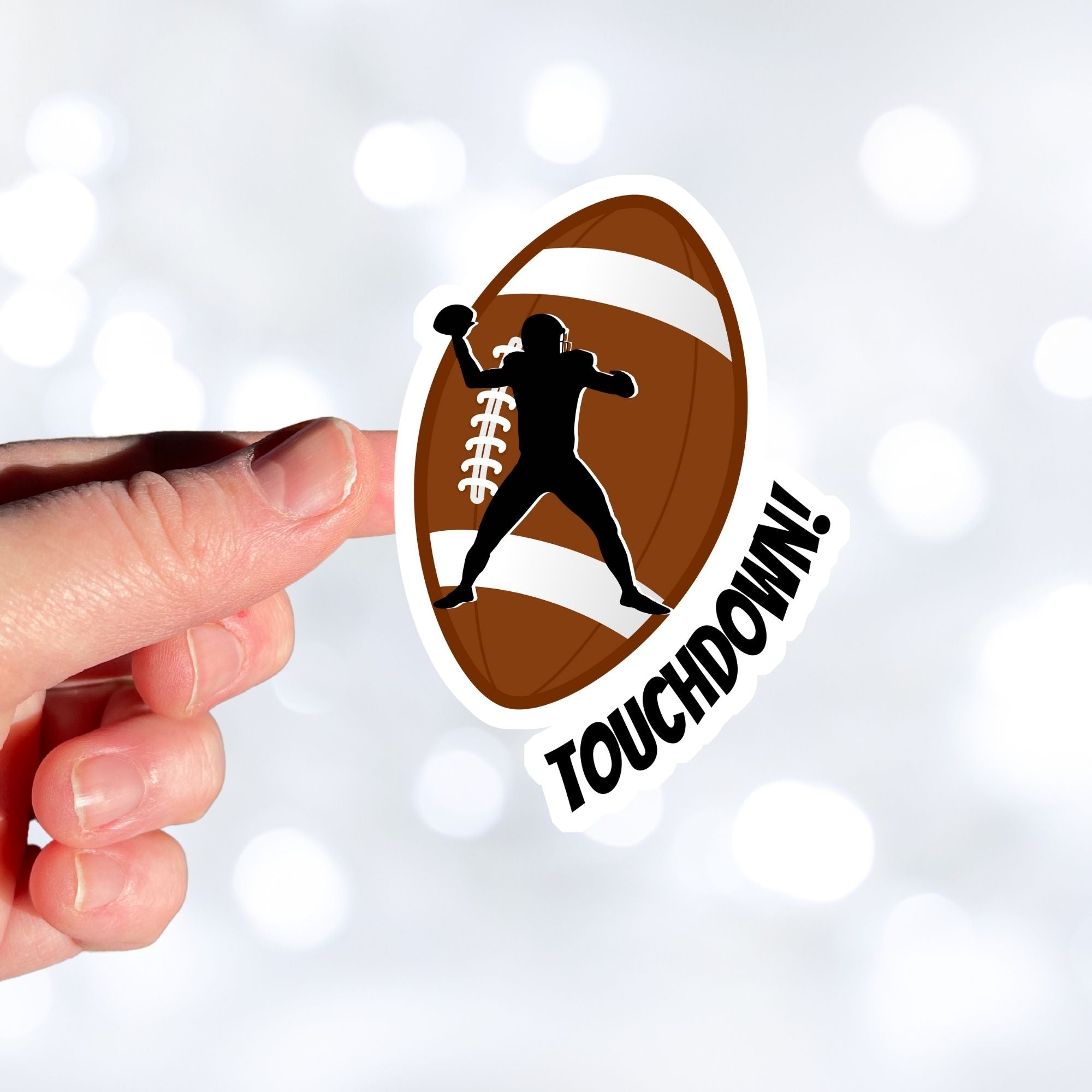 This individual die-cut sticker features the silhouette of a football (American) player about to pass the ball, on a football background, with the word "Touchdown!" on the lower right side. This image shows a hand holding the touchdown sticker.