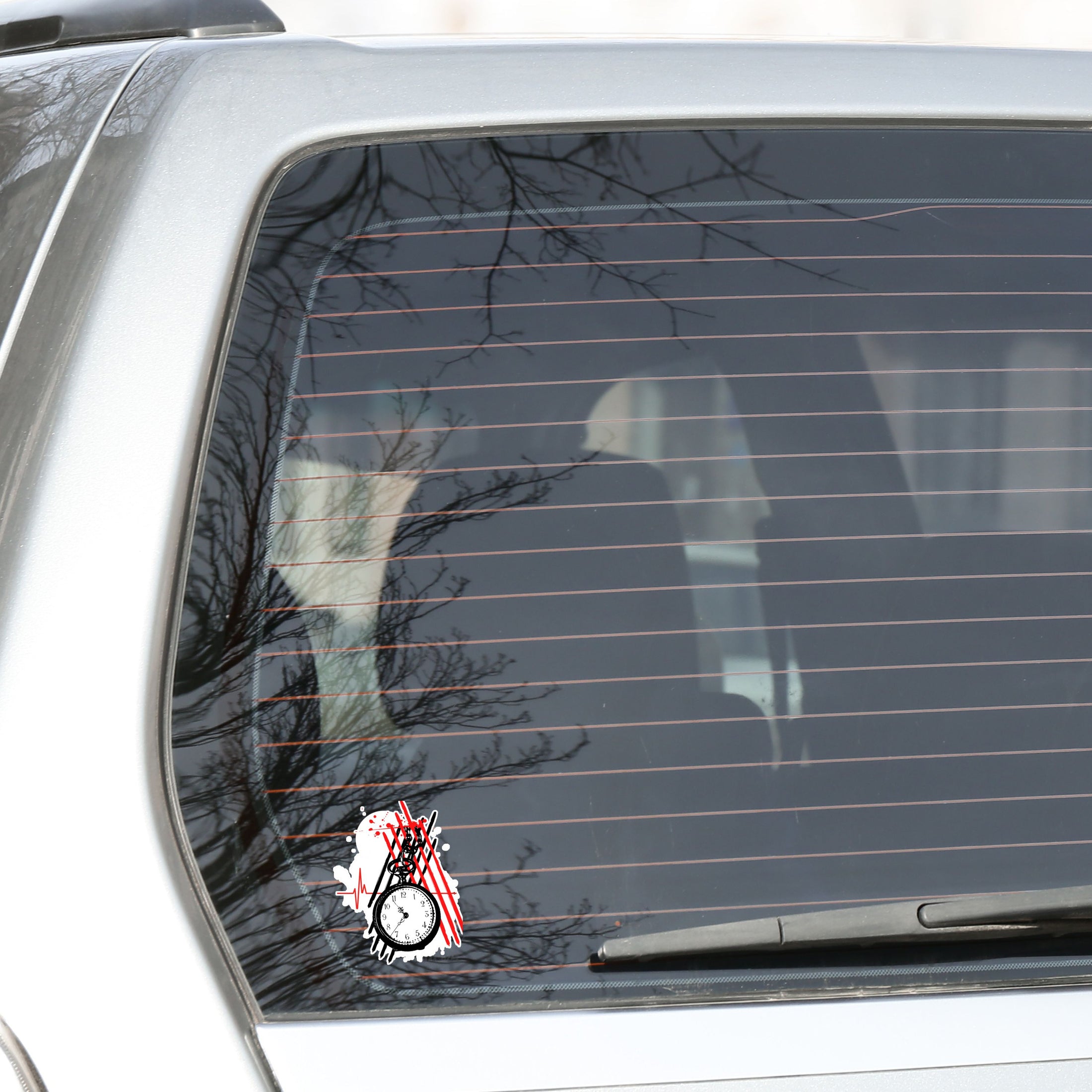 Trash Polka uses red, black, and white with a combination of abstract, surrealistic, and realistic images, and this individual die-cut sticker features a black and white pocket watch with red and black stripes behind.  This image shows the trash polka pocket watch sticker on the rear window of a car.