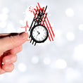 Load image into Gallery viewer, Trash Polka uses red, black, and white with a combination of abstract, surrealistic, and realistic images, and this individual die-cut sticker features a black and white pocket watch with red and black stripes behind.  This image shows a hand holding the trash polka pocket watch sticker.
